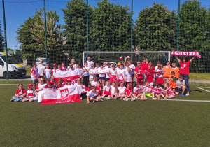 Duża grupa uczniów SP 5 wraz z 5 nauczycielami pozuje w strojach kibiców przed bramką na boisku szkolnym.