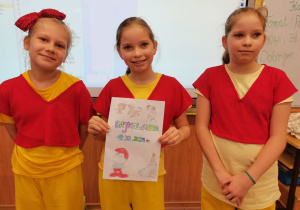 Trzy dziewczynki trzymają laurkę z życzeniami