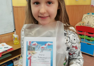 Lenka prezentuje nagrodę otrzymaną w szkolnym konkursie plastycznym "Pocztówka z Ozorkowa"..