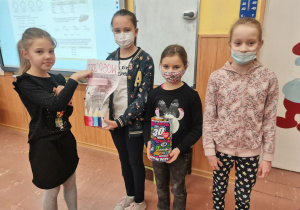 Trzy dziewczynki z Samorządu Szkolnego trzymają puszki. Uczennica z klasy II b wrzuca pieniądze do puszki.
