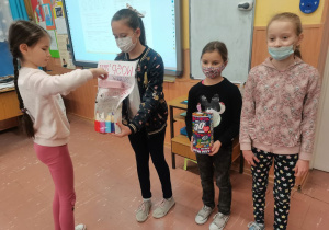 Trzy dziewczynki z Samorządu Szkolnego trzymają puszki. Uczennica z klasy II b wrzuca pieniądze do puszki.
