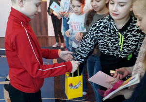 Chłopiec częstuje dziewczynki słodkim batonikiem.