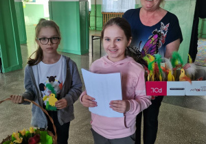 2 dziewczynki wraz z opiekunką samorządu szkolnego składają życzenia pracownikom szkoły.