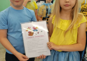 Dwoje dzieci w strojach bajkowych pokazuje kartę z życzeniami.