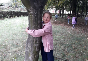 Dziewczynka przytula się do drzewa.