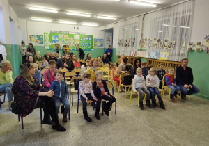 Uczestnicy Dnia Otwartego siedzą w holu szkoły.