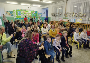 Uczestnicy Dnia Otwartego siedzą w holu szkoły.