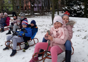 Uczniowie w parach zjeżdżają z górki na sankach.