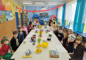 Uczniowie klasy III w strojach karnawałowych przy stole z przekąskami