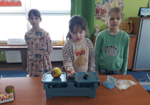 Dziewczynka waży jabłko, a kolejna uczennica będzie ważyć gruszkę