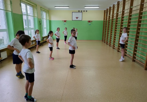 Uczennica pokazuje propozycje ćwiczeń, koledzy ćwiczą.