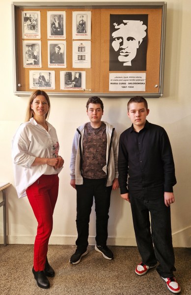 Od lewej: nauczycielka języka angielskiego p. I. Zimińska, uczniowie klasy 8b: Arkadiusz Wichliński i Mateusz Kaźmierczak na tle gabloty z wizerunkiem patronki szkoły Marii Curie-Skłodowskiej.