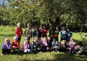 Uczniowie pozują z jabłkami pod jabłonką.