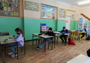 Uczniowie siedzą w ławkach i piszą tekst konkursu ortograficznego.