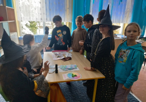 Grupa dzieci stoi przy stoliczku i czeka na wróżby