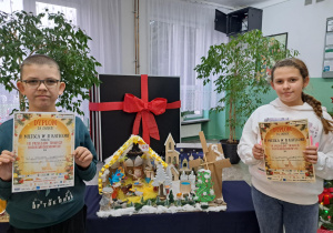 Dzieci prezentują dyplomy stojąc przy szopce.