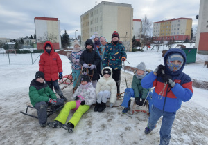Uczniowie stoją z sankami na szczycie górki