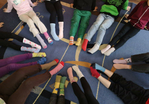 Uczniowie 1b siedzą w kole pokazując różnokolorowe skarpety.