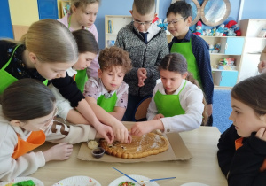 Dzieci ozdabiają duży mazurek w kształcie pisanki.