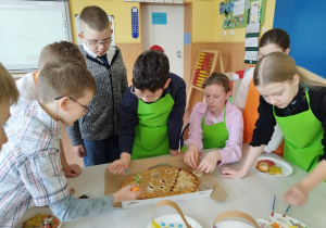 Dzieci ozdabiają duży mazurek w kształcie pisanki.