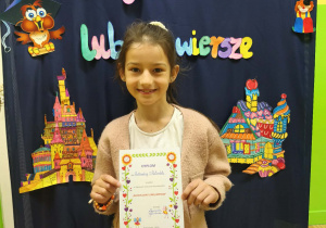 Uczennica trzyma dyplom za udział w szkolnym konkursie recytatorskim "Bajkoludki lubią wiersze"