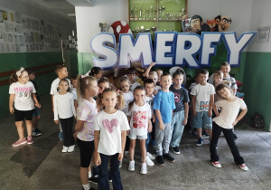 Uczniowie stoją przy banerze Smerfy.