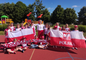 Uczniowie z klasy "Jagódki" wraz z wychowawczynią pozują na boisku Bajkolandii w strojach kibiców polskiej reprezentacji.