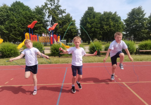 3 dzieci skacze na skakankach na boisku szkolnym