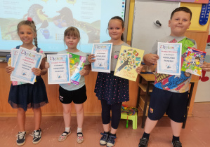 Czworo dzieci trzyma dyplomy oraz nagrody książkowe za klasowy Konkurs Piosenki