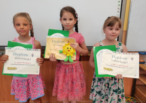 Trzy dziewczynki trzymają dyplomy i nagrody za klasowy Konkurs Ortograficzny