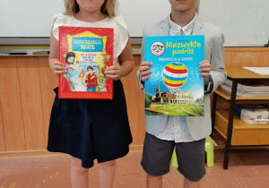 Dwoje dzieci trzyma dyplomy i nagrody książkowe za szkolny Konkurs Recytatorski