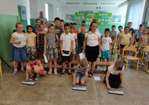 3 dzieci z klasy I gra "Sto lat" na cymbałkach, pozostali uczniowie Bajkolandii śpiewają, stojąc za nimi