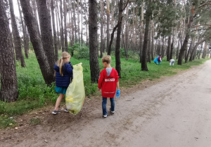 Czworo dzieci uprząta teren w lasku miejskim.