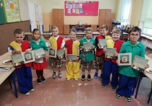 Dzieci w strojach Gumisiów stoją w klasie i pokazują upominki imieninowe - książki.