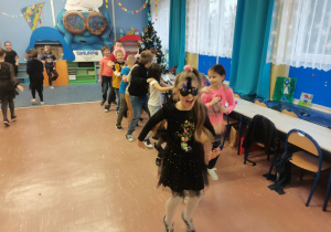 Grupa dzieci tańczy tworząc węża na środku klasy.