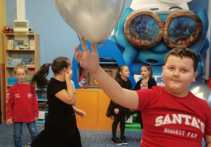 Grupa dzieci tańczy na środku klasy. Chłopiec trzyma balonik.