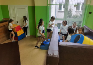 Dziewczynki budują "dom" z materacy do ćwiczeń gimnastycznych.