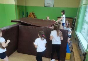 Dziewczynki budują "dom" z materacy do ćwiczeń gimnastycznych.