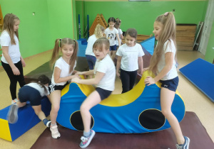 Dziewczynki budują "plac zabaw" z materacy do ćwiczeń gimnastycznych.