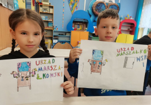 Dwoje dzieci prezentuje swoje prace konkursowe.