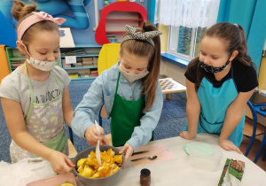 Dzieci pracują w grupach nad wykonaniem sałatki owocowej.