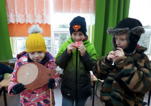 Trzech uczniów w strojach zimowych prezentują dawny sposób odżywiania się z ludności eskimoskiej.