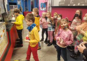 Dzieci w kolorowych strojach stoją w holu kina, robią zakupy przed seansem.