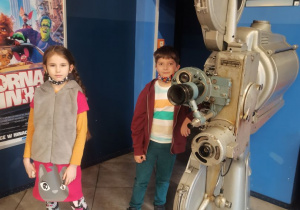 2 dzieci pozuje do zdjęcia w holu kina przy dużym projektorze.