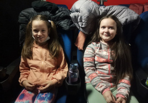 2 dziewczynki siedzą w sali kinowej. Czekają na projekcję filmu.