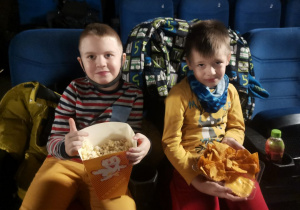 2 chłopców siedzi w sali kinowej. Czekają na projekcję filmu.