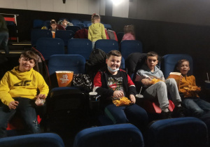 4 chłopców siedzi w sali kinowej. Czekają na projekcję filmu.