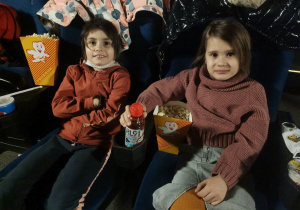 2 dziewczynki siedzą w sali kinowej. Czekają na projekcję filmu.