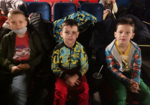 3 chłopców siedzi w sali kinowej. Czekają na projekcję filmu.
