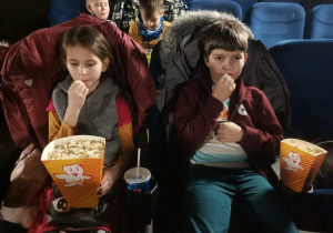 2 dzieci siedzi w sali kinowej. Czekają na projekcję filmu.